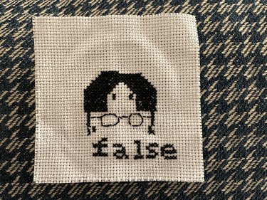 A cross-stitch of Dwight Shrute (character from "The Office" television show) with the word "false" below his face