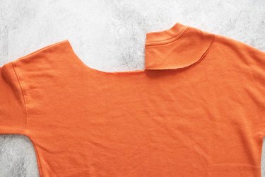 Cutting neckline of orange sweatshirt on a gray background