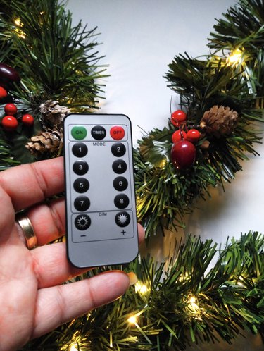 Hand holding remote control over green garland
