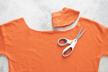 Cutting neckline of orange sweatshirt on a gray background