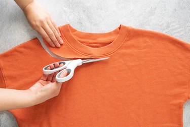 Cutting neckline of orange sweatshirt on a gray background