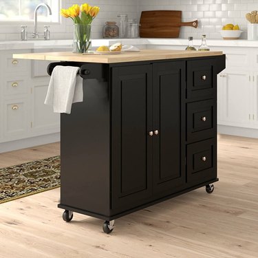 Black kitchen cart with an oak countertop on four wheels with locking mechanisms.