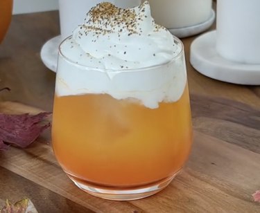 Glass filled with orange-colored mocktail and topped with whipped cream