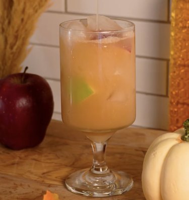 Light orange cocktail filled with apple chunks and ice cubes