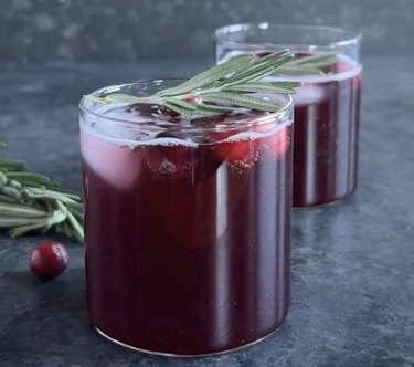 Two glasses filled with dark red cocktail and a sprig of rosemary