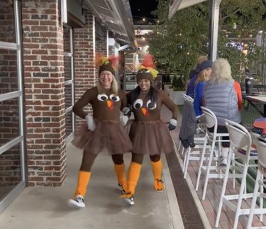 Two women dressed in homemade brown-and-orange turkey costumes