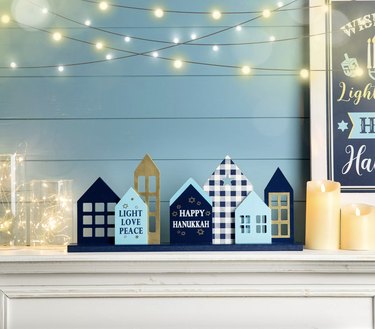 Blue and white Hanukkah houses on fireplae mantel. One house says "Happy Hanukkah" and another says "Light Love Peace."