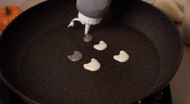 Piping mini cat pancakes on nonstick pan