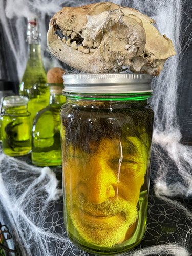 head in a specimen jar with raccoon skull on top