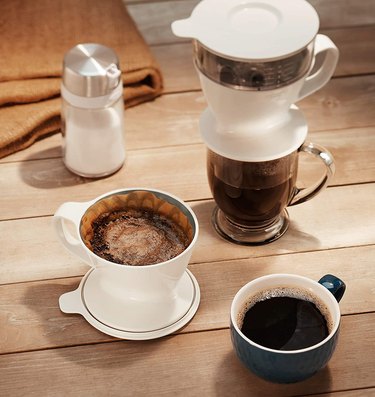 OXO pour-over coffee maker on a wood slat table next to a coffee cup and creamer.