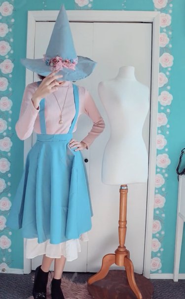 Woman wearing a witch costume made with light blue and pastel pink fabric, including an embellished blue witch hat
