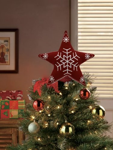 Red fabric star tree topper with white embroidery that looks like snowflakes.