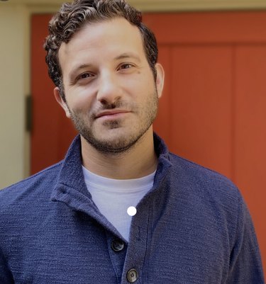 A headshot of Rob Sayegh Jr. in a blue button-down shirt in front of a red door