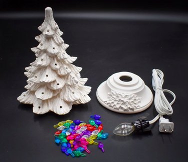 A white ceramic Christmas tree, base, colorful lights, and cord with lightbulb