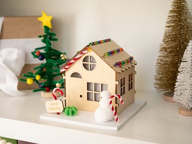 A wooden house with candy canes on the outside, a snowman, and a pipe cleaner Christmas tree.