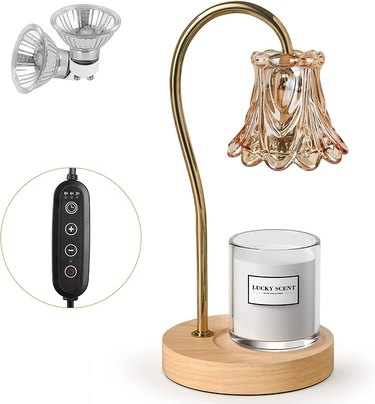 Candle warmer lamp with a tulip-inspired glass shade in a dusty rose color, a gold-finished arm, and a light wood base.