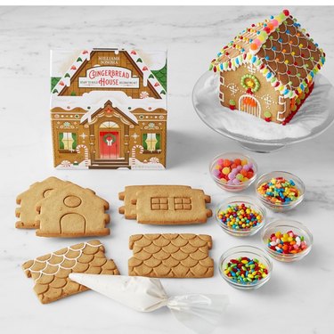 Williams-Sonoma gingerbread house kit shown on a marble countertop in its retail packaging, with all the pieces laid out for viewing, and fully constructed