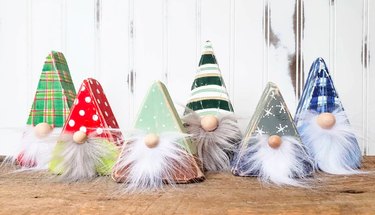 Six triangle-shaped wooden gnomes with fluffy white and gray beards in various holiday colors and prints, including red, blue, amd green stripes, plaids, and stars