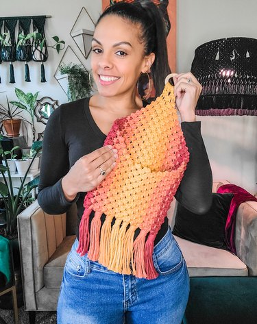 Casey Alberti holding a beautiful macrame creation with reds, oranges and yellows