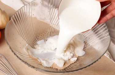 Pouring milk and oil into a bowl with yeast and sugar.