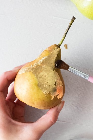 Brushing away extra gold leaf from pear