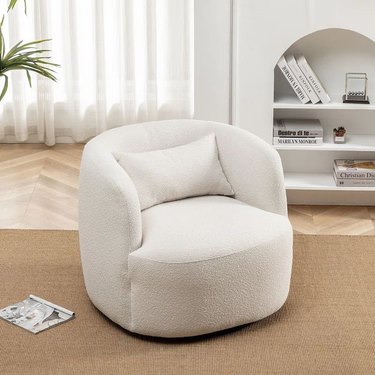 White boucle swivel chair with toss pillow and rounded edges.