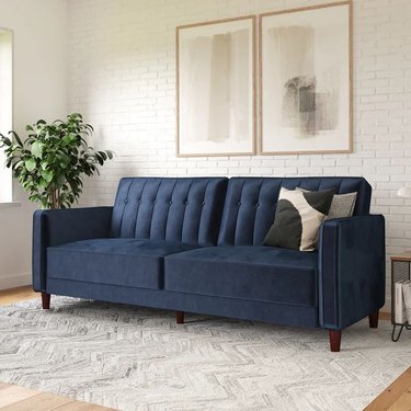 Navy blue tufted velvet sofa that folds flat to create a twin-sized sleeping surface.