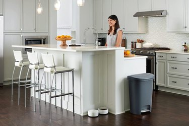 Rubbermaid kitchen trash can, in grey, shown at the end of the island in a sleek, modern kitchen