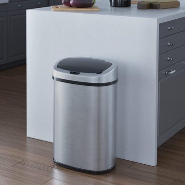 iTouchless sensor trash can, in brushed stainless steel, pictured against the stone "waterfall" edge of an upscale kitchen island.