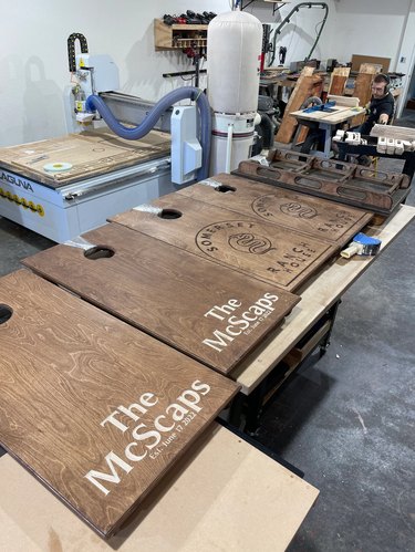 Four completed wooden cornhole boards. The first two are engraved with "The McScaps" in white lettering, while the other two read "Ranch House"