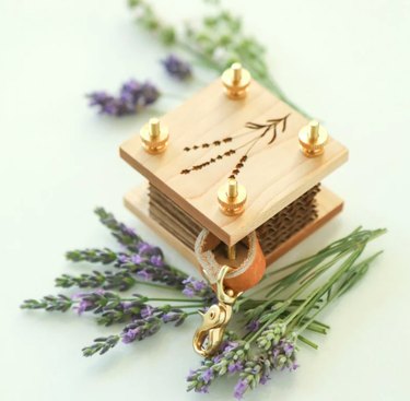 A miniature square flower press with a lavender engraved illustration and a leather and brass keychain ring.
