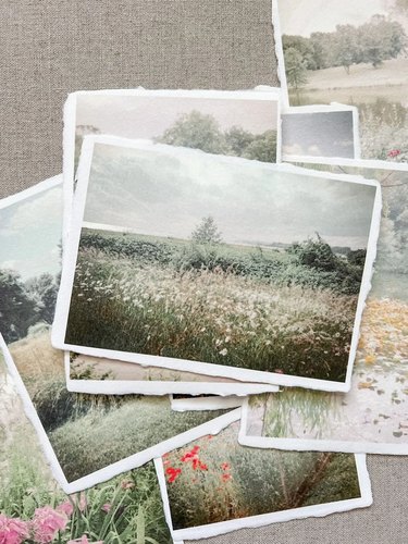 A pile of digital nature photos, including a field of white flowers and red and pink blooms, printed on handmade cotton paper