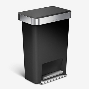 Simplehuman kitchen trash can in black with stainless steel rim, shown slightly shadowed on a white surface