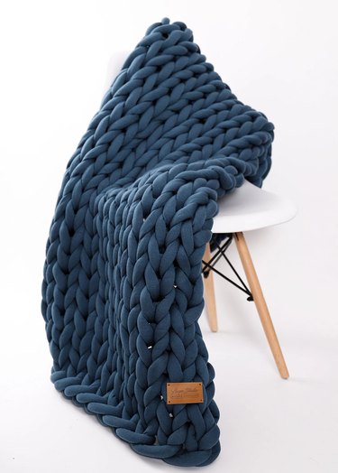 A thick and chunky navy-blue blanket draped over a white chair