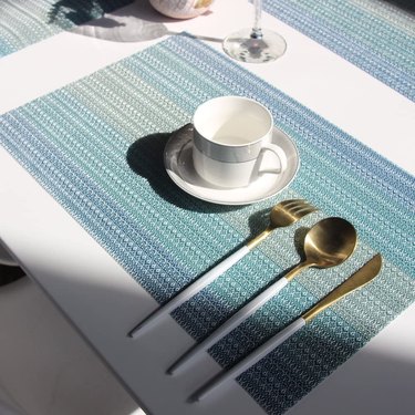 Bright Dreams placemats in a variegated blue weave, shown on a patio table with silverware, tea cup and wine glass