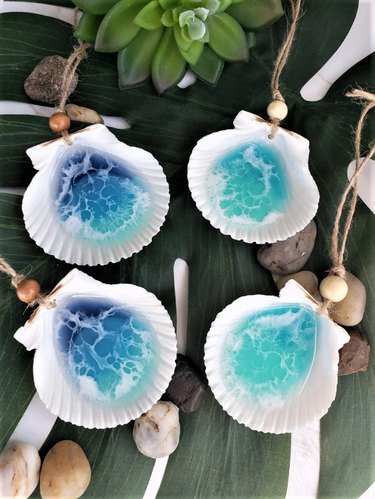 Set of four ornaments made from white seashells. Two shells are filled with light turquoise resin, while the other two are filled with darker blue resin. The resin resembles ocean waves.