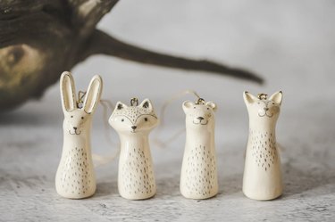 A set of four white ceramic ornaments (a bunny, fox, bear and raccoon) with lightly painted gray faces.