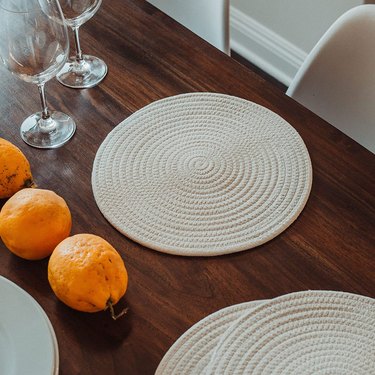 Organihaus round placemats on a dark wood tabletop, shown with wine glasses and fresh oranges