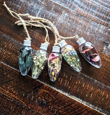 A set of five plastic mini lightbulb-shaped ornaments filled with dried flowers and eucalyptus.