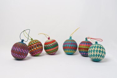Six vibrant woven string ball ornaments in a variety of colors, including several with rainbow stripes.