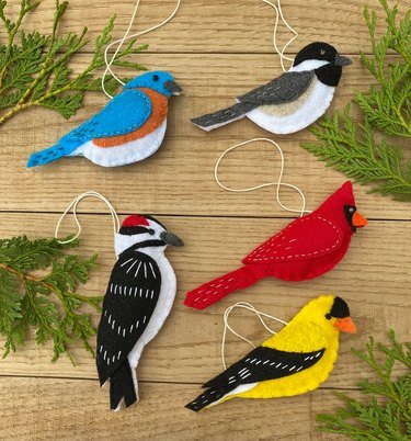 A set of five felt bird ornaments. They include a red cardinal, a chickadee, a bluebird, a woodpecker and a goldfinch.