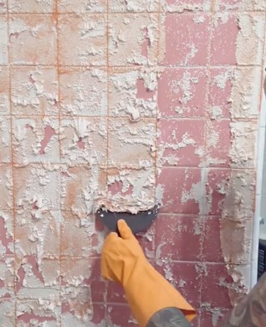 Hand in orange glove scraping paint off pink tile