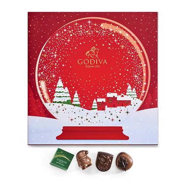 Godiva advent calendar in a red box with a glittery snowglobe on it. Four of the included chocolate shapes are shown below the calendar.