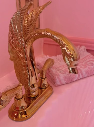 Gold swan-shaped sink fixture over pink sink