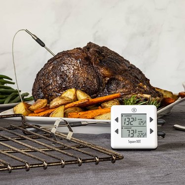 ThermoWorks Square Dot thermometer, pictured in front of a large roast garnished with vegetables, and with the air-temp probe clipped to an oven rack in the foreground