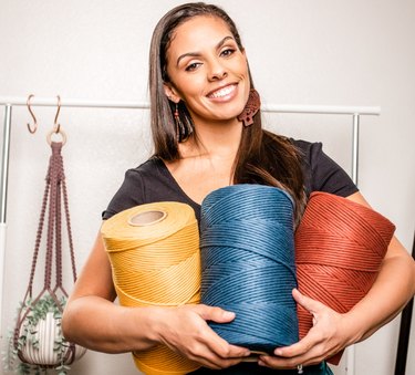 Casey Alberti holding rolls of yellow, blue and red thread