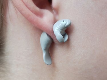 A white-skinned ear wearing an earring shaped like a gray manatee. The manatee appears to be cut in half with the person's earlobe in the middle.