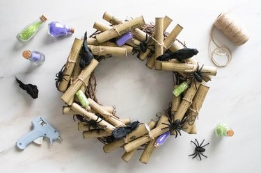 Hot glue faux spiders, crows and mini potion bottles on potion scroll wreath