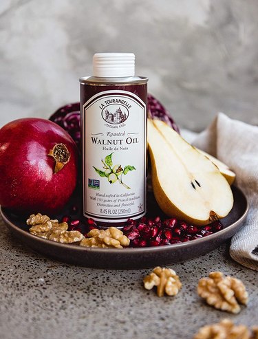 La Tourangelle walnut oil, shown on a stone countertop in a shallow plate that also contains walnuts, a pear, and a couple of pomegranates