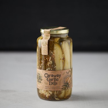 An unopened jar of caraway dill pickles from The Real Dill, shown on a grey counter with a black background